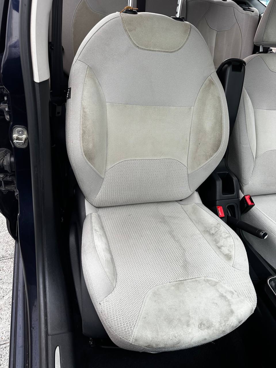 Sedile anteriore di un'auto in tessuto grigio chiaro con aloni scuri su schienale e seduta